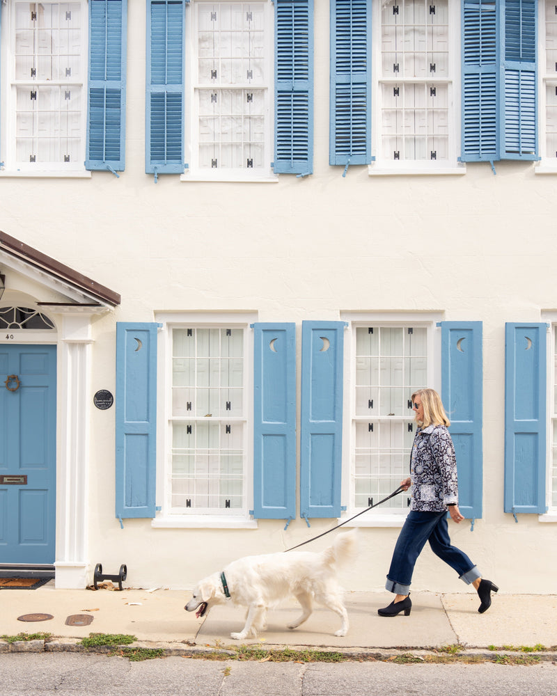 Woman walking a dog on a leash in front of a house with blue shutters.